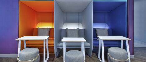Une pièce comprenant trois espaces de détente, chacun avec une table et un pouf, ainsi qu’un espace de détente central avec une chaise et une table.