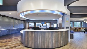 Un espace d’accueil moderne, avec un comptoir d’accueil incurvé, un grand luminaire circulaire et un coin salon offrant une vue sur l’extérieur.