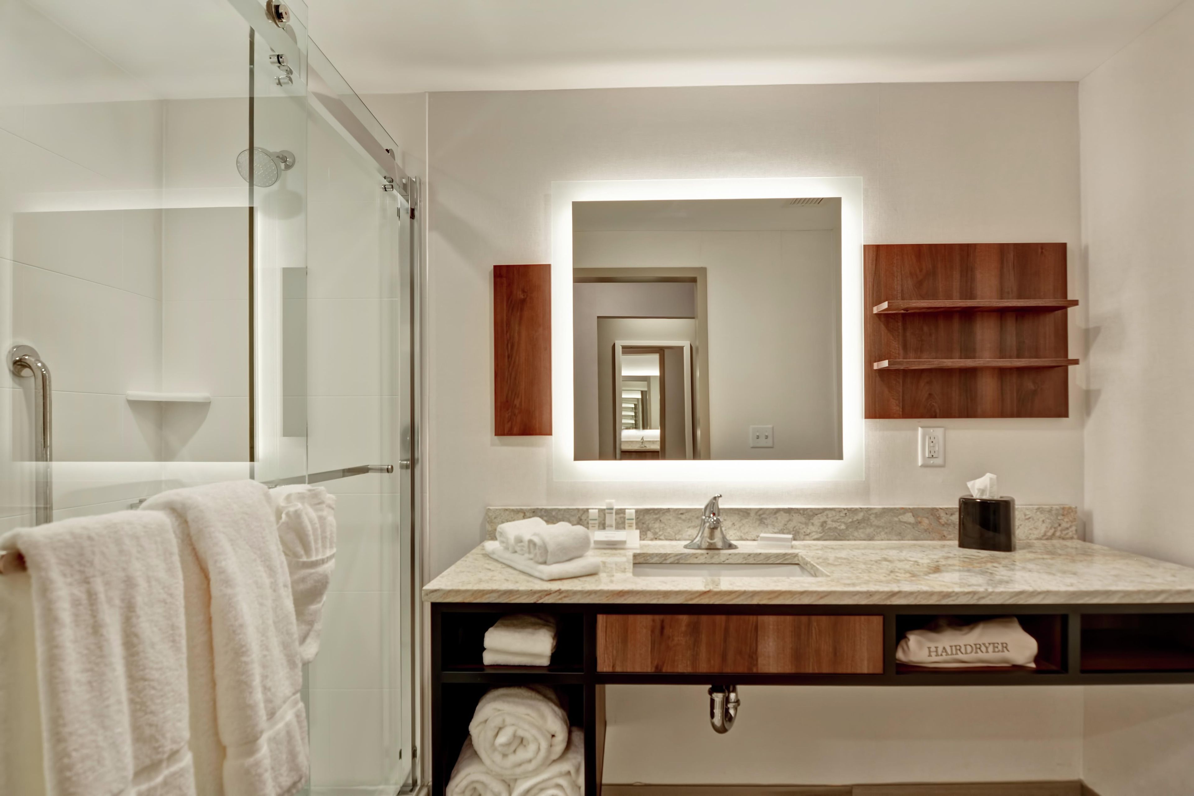 Een moderne badkamer met een douchecabine van glas, een wastafel met een marmeren blad en houten kastjes.