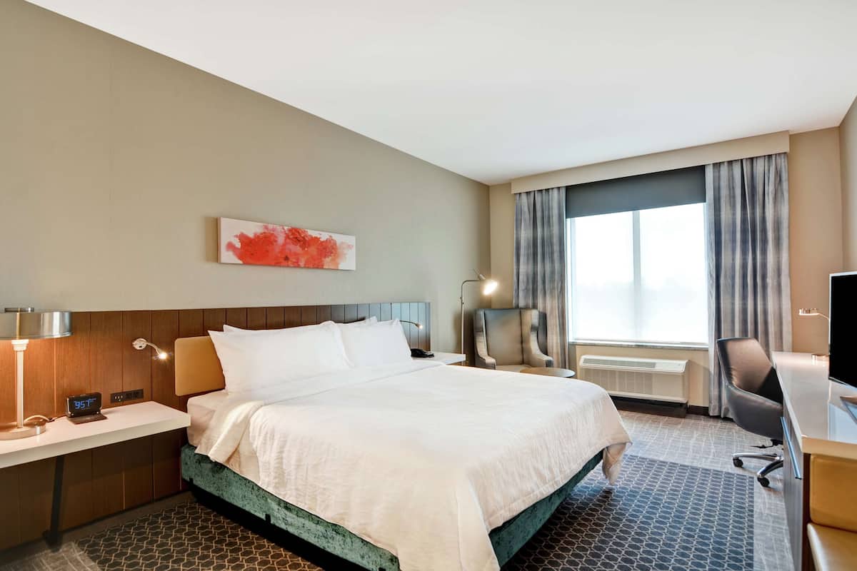 A hotel room with a large bed, a desk, a chair, a TV, and a window with curtains.