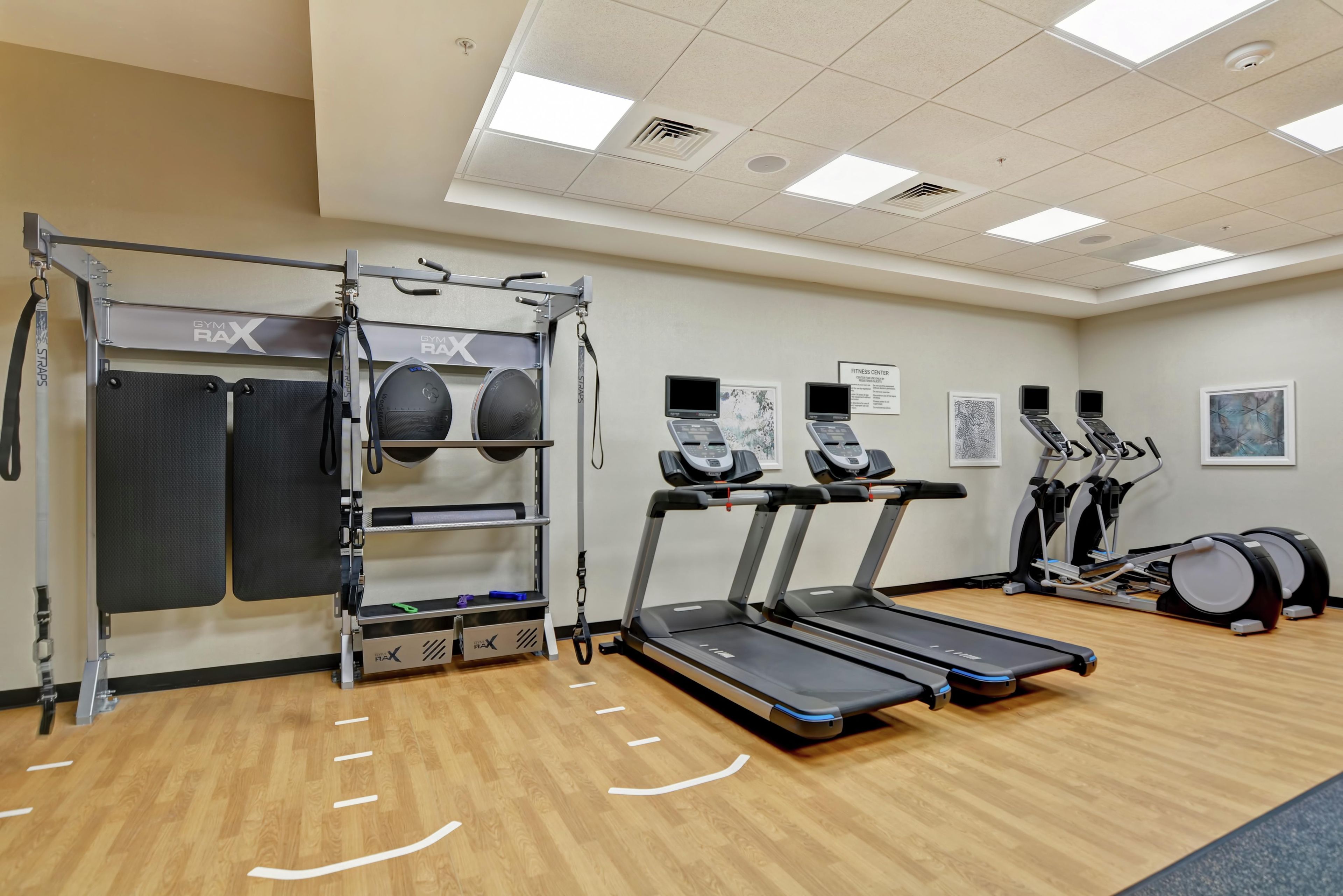 Un gimnasio con cintas de correr, barra de dominadas y una máquina de ejercicios de pared.