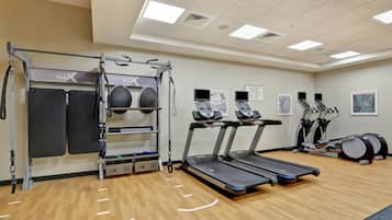 Un gimnasio con cintas de correr, barra de dominadas y una máquina de ejercicios de pared.