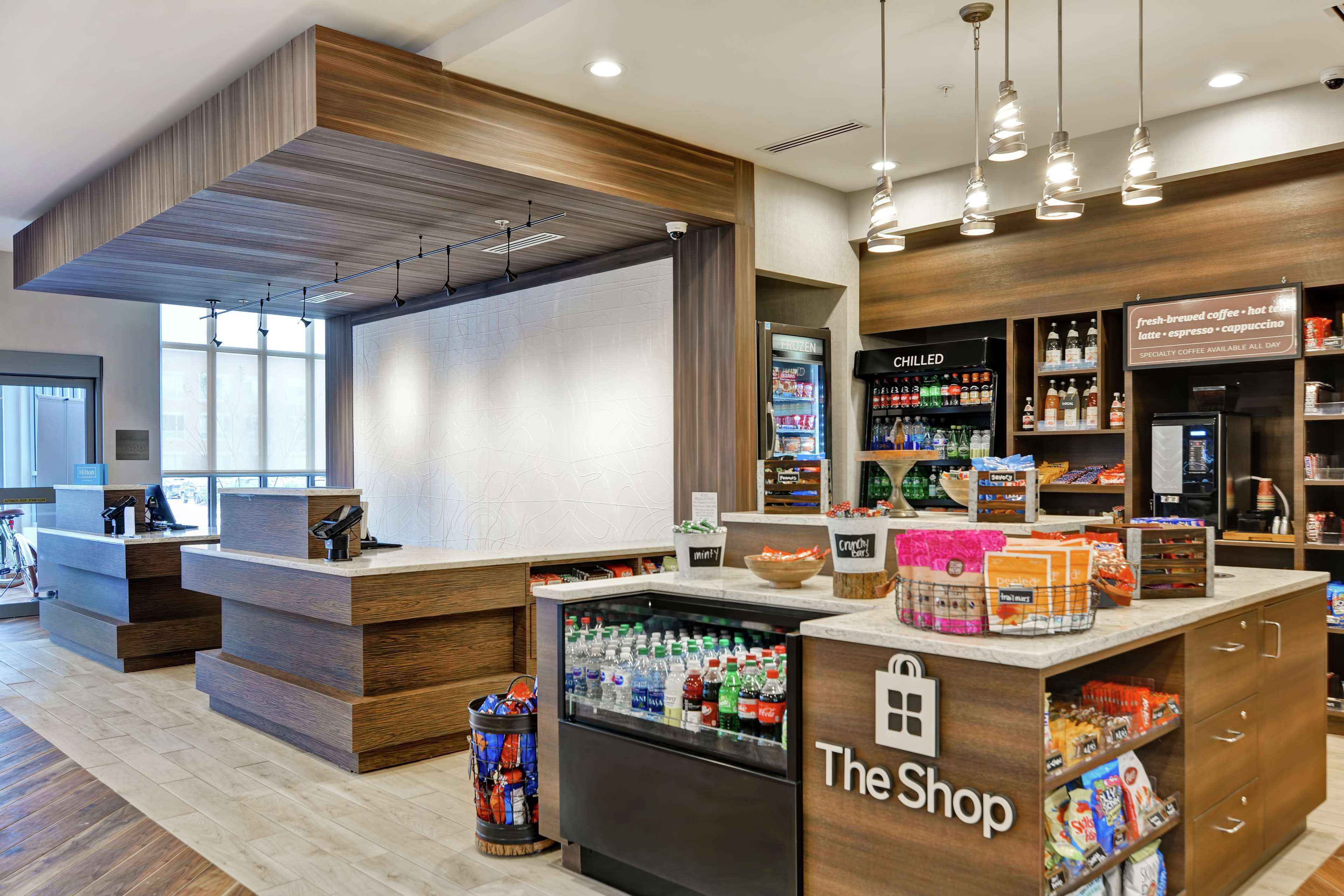 A modern coffee shop interior with a counter, refrigerated display, and shelves stocked with beverages and snacks.