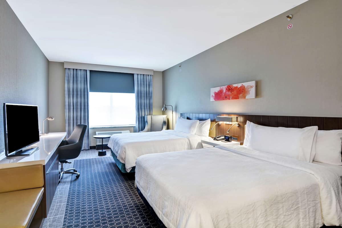 A hotel room with two beds, a desk with a TV, a chair, and a window with curtains.