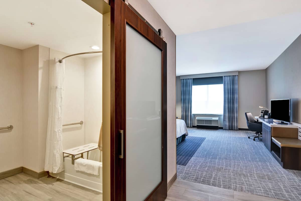 A hotel room with a shower, a bed, a desk, and a television.