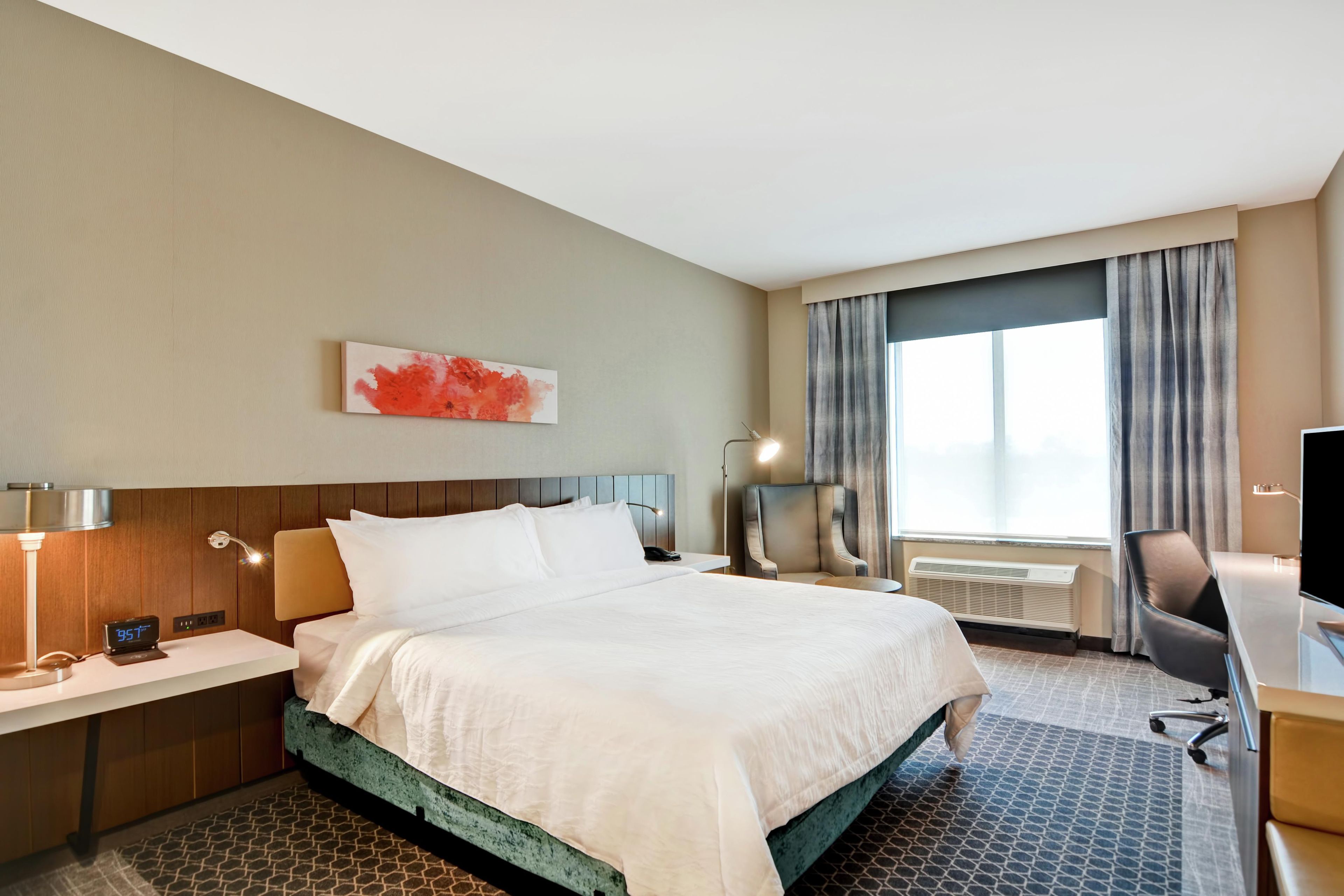 Een hotelkamer met een bed, een bureau, een stoel, een televisie en een raam met gordijnen.