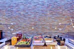 Ein reichhaltiges Buffet mit verschiedenen Speisen und Getränken vor einer rustikalen Ziegelwand.