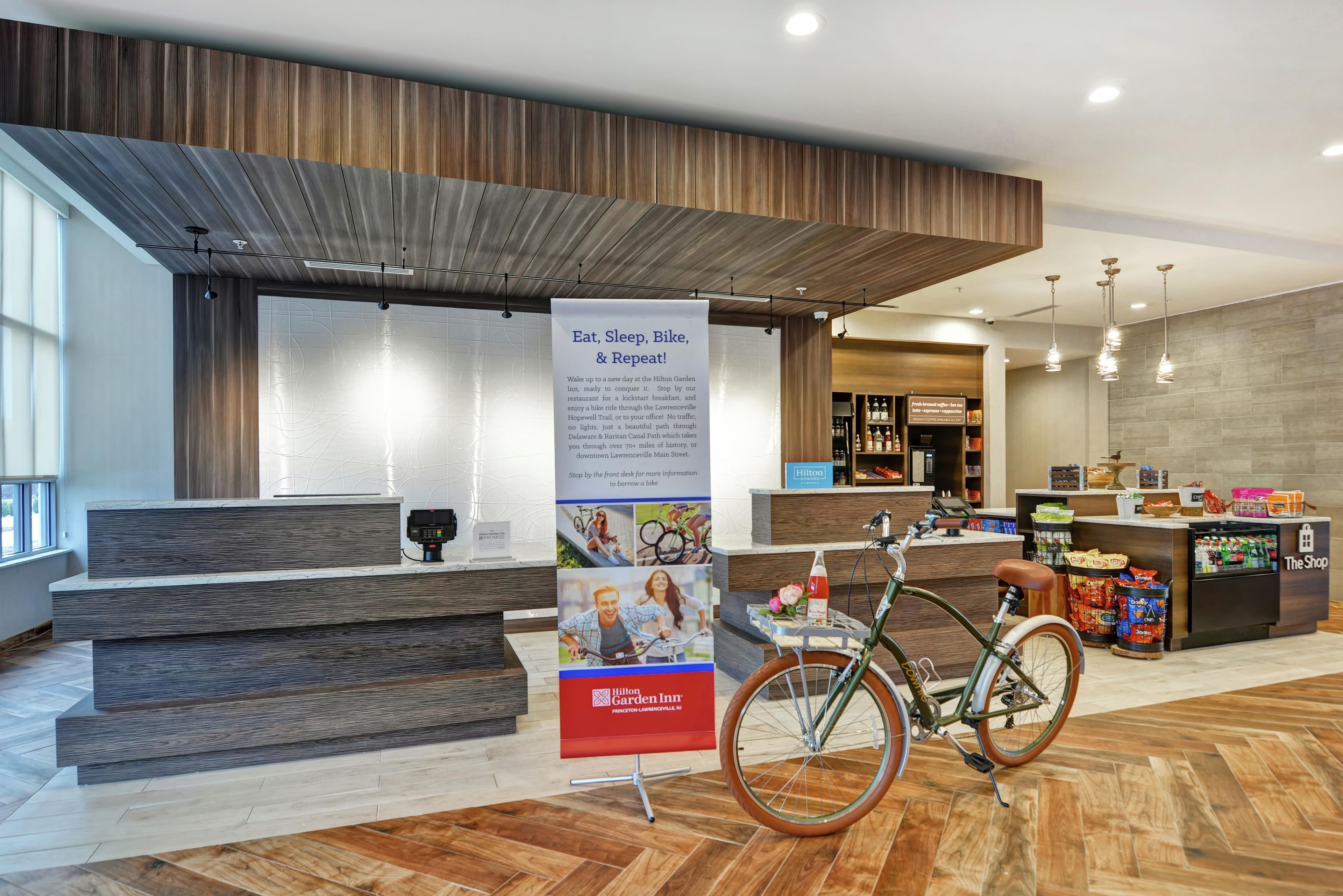 Zona de recepción de un hotel con un mostrador de madera, una bicicleta estacionada adelante y un cartel que promociona actividades locales.