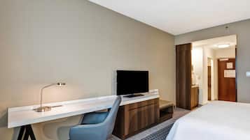 Ein Hotelzimmer mit einem Bett, einem Schreibtisch mit Stuhl, einem Fernseher und einem durch eine offene Tür einsehbaren Badezimmer.
