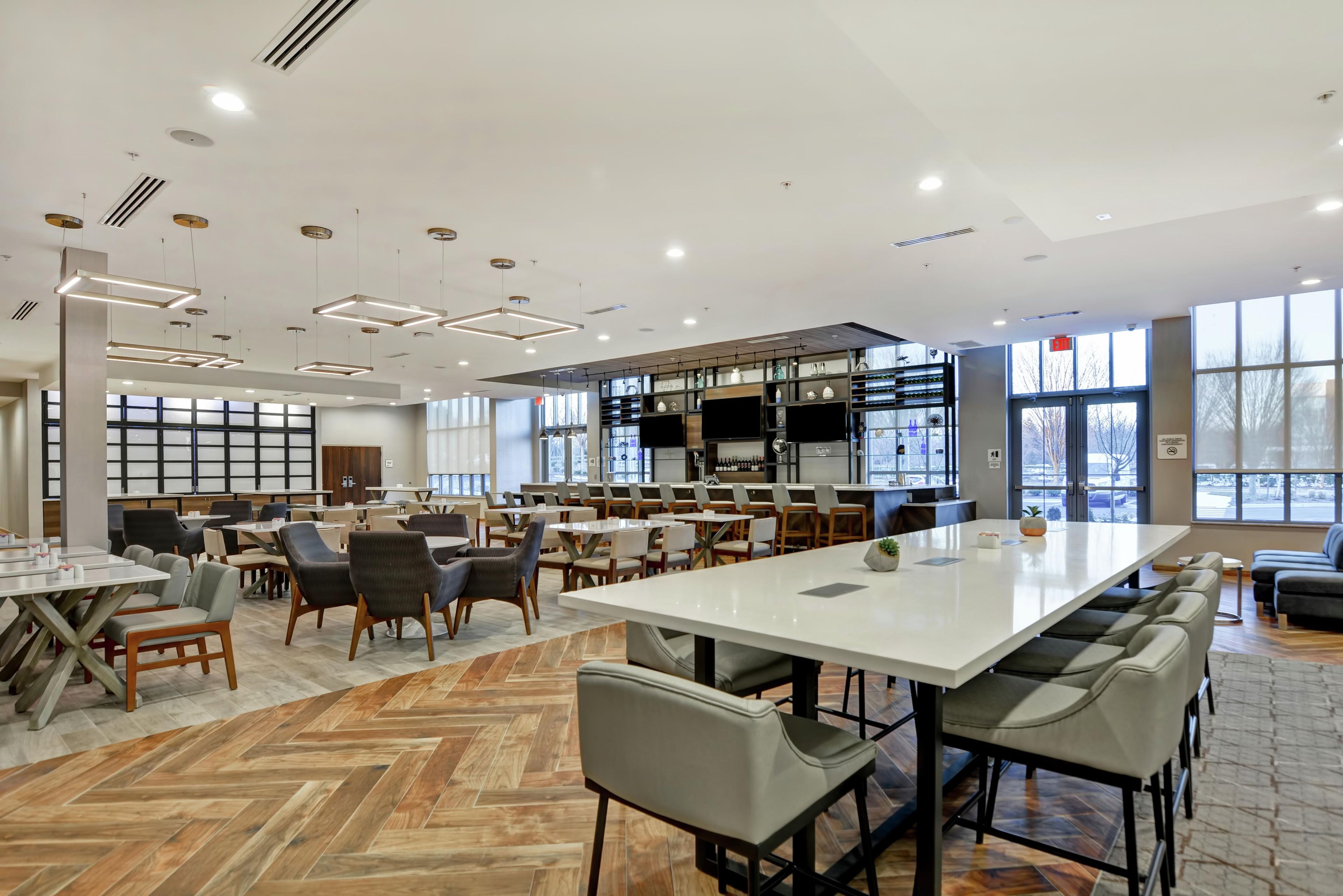 A spacious indoor area with multiple seating arrangements, a long table, and a bar area with shelves.