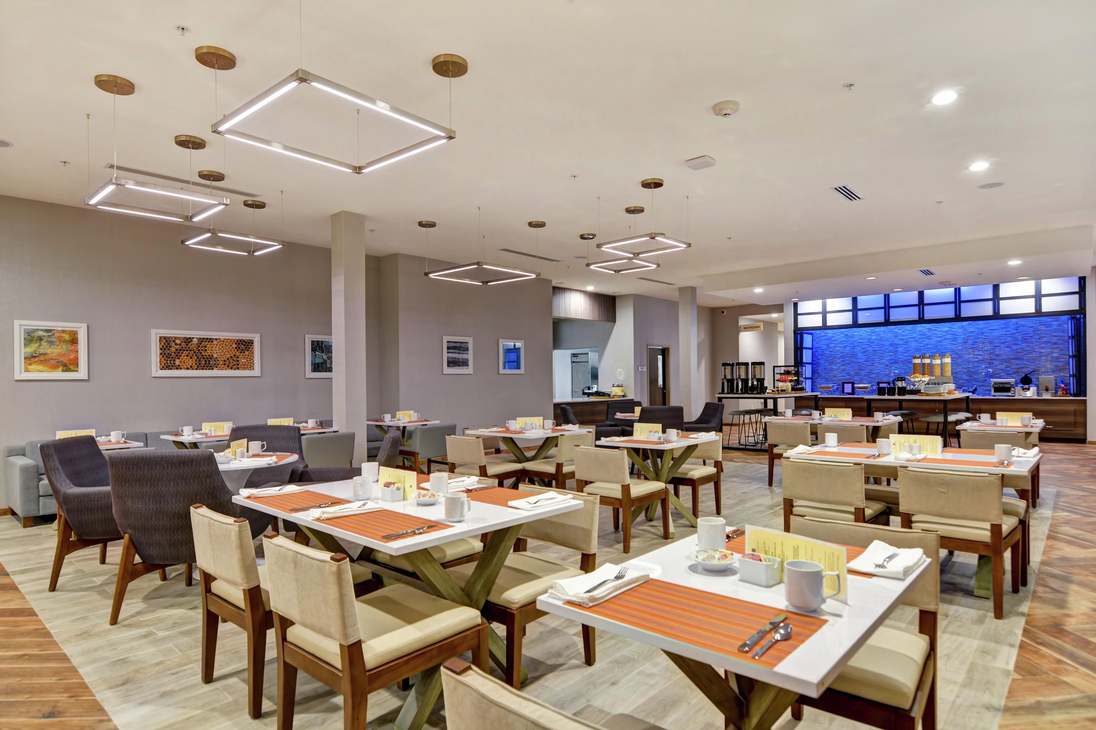Un comedor moderno con varias mesas y sillas, una cocina al fondo y obras de arte en las paredes.