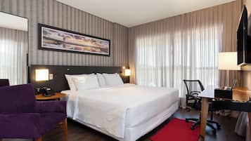 Habitación de hotel con una cama grande, un escritorio, una silla, un televisor y un cuadro en la pared.