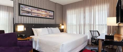 A hotel room with a large bed, a desk, a chair, a TV, and a painting on the wall.
