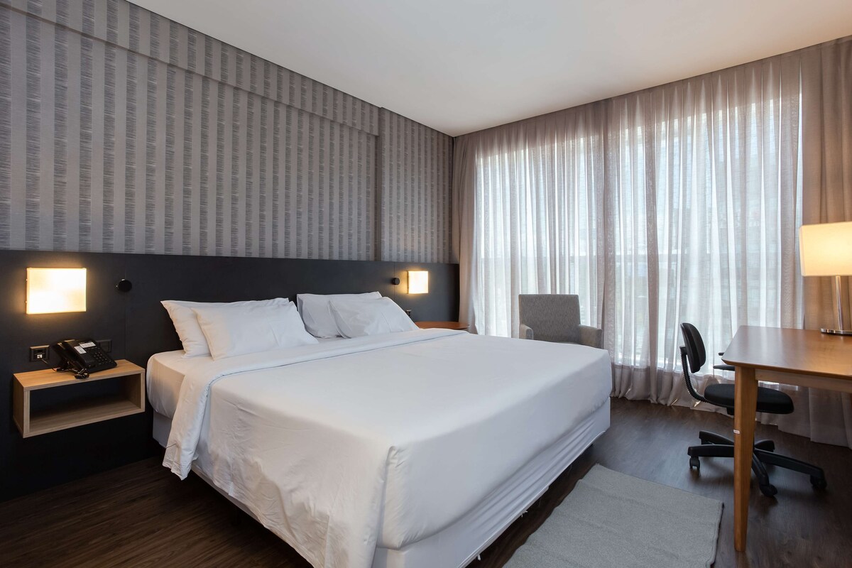 A hotel room with a large bed, bedside lamps, a desk, and a chair.