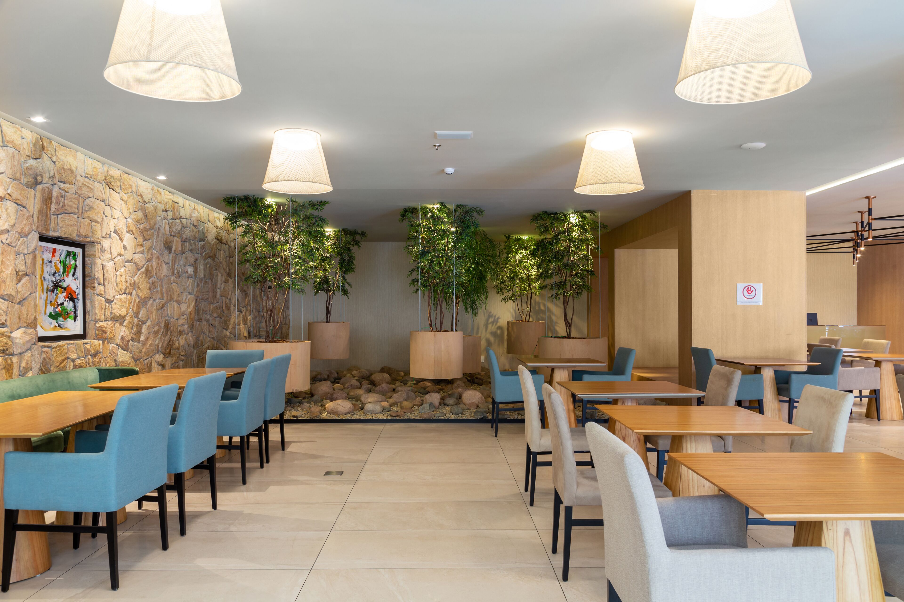 A modern dining area with stone walls, wooden tables, and blue chairs.