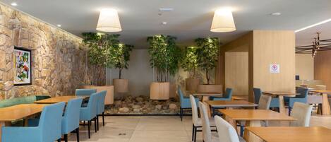 A modern dining area with stone walls, wooden tables, and blue chairs.