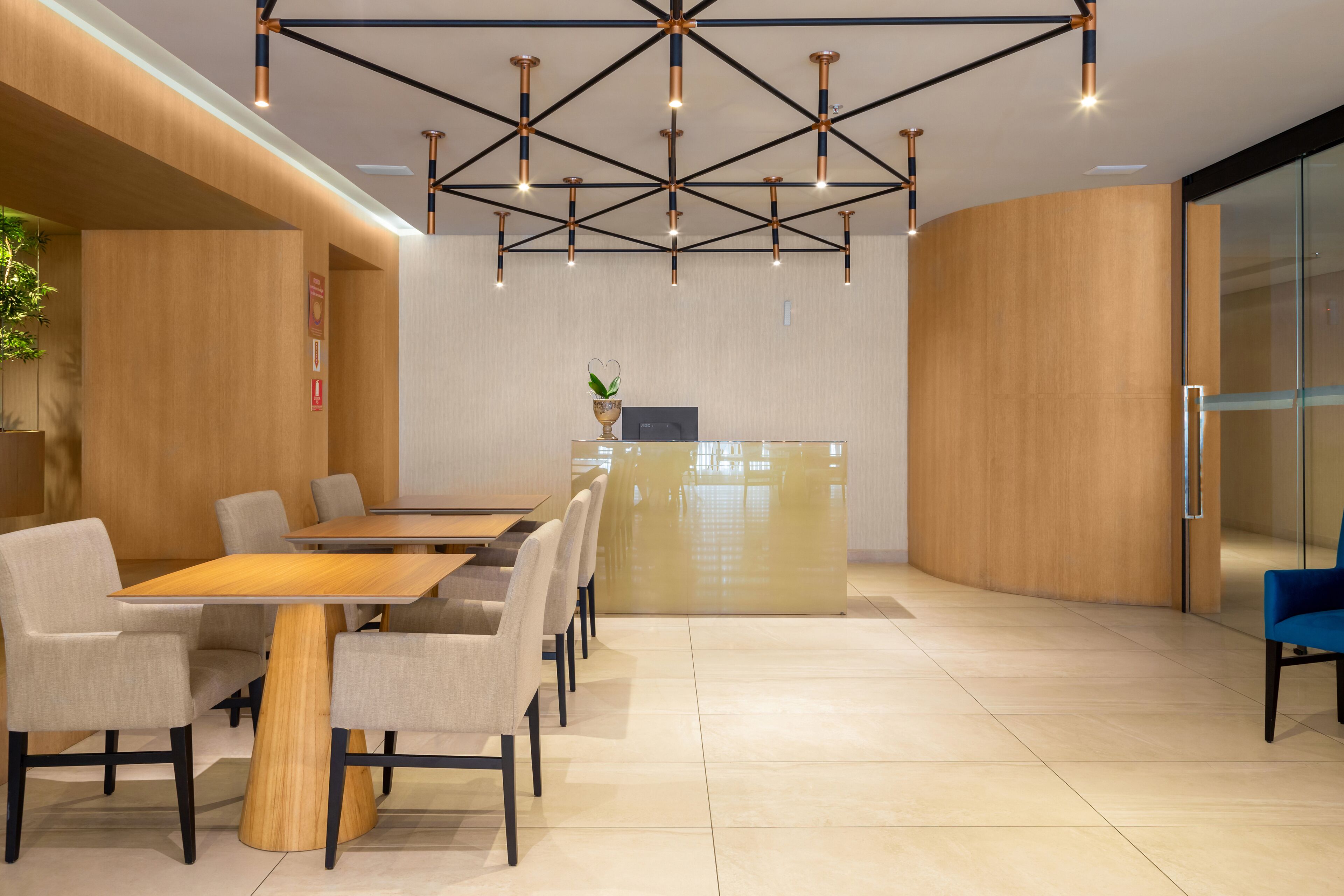 Une salle de conférence moderne, dotée d’une table et de chaises en bois, d’un comptoir d’accueil et d’un plafond au design géométrique.