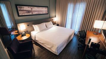 Habitación de hotel con una cama grande, un escritorio con silla, una mesita y un teléfono.