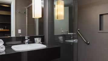 A modern bathroom with a glass shower enclosure, a black countertop, a white sink, and a large mirror.