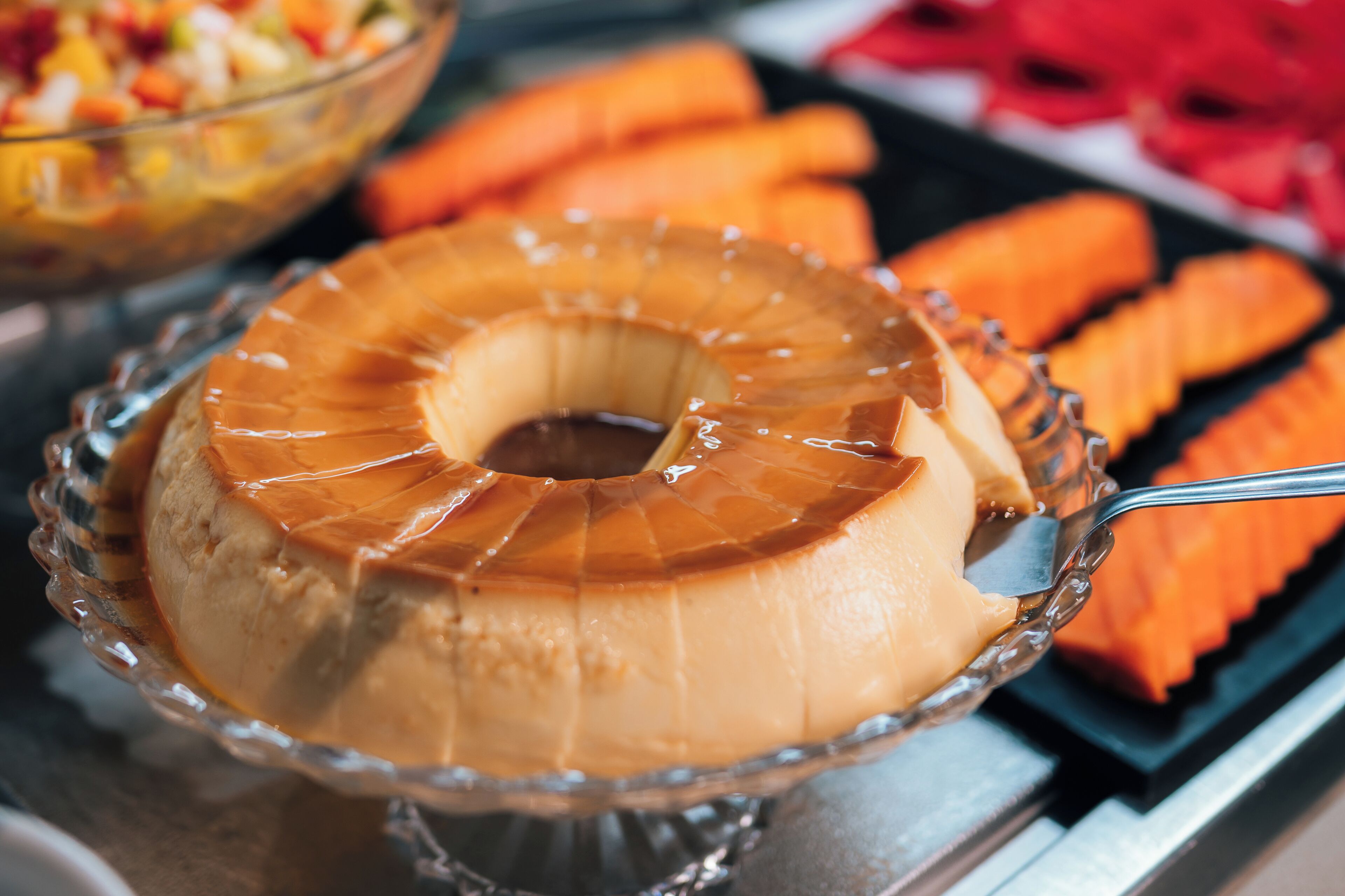 A caramel flan in a glass dish with a spoon, surrounded by other desserts.