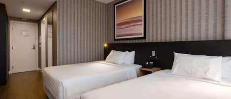 A hotel room with two beds, a large framed picture on the wall, and a wooden floor.