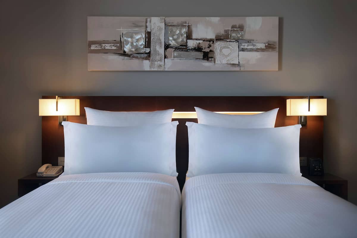 A hotel room with a large bed, two bedside lamps, a phone on the nightstand, and a painting on the wall.