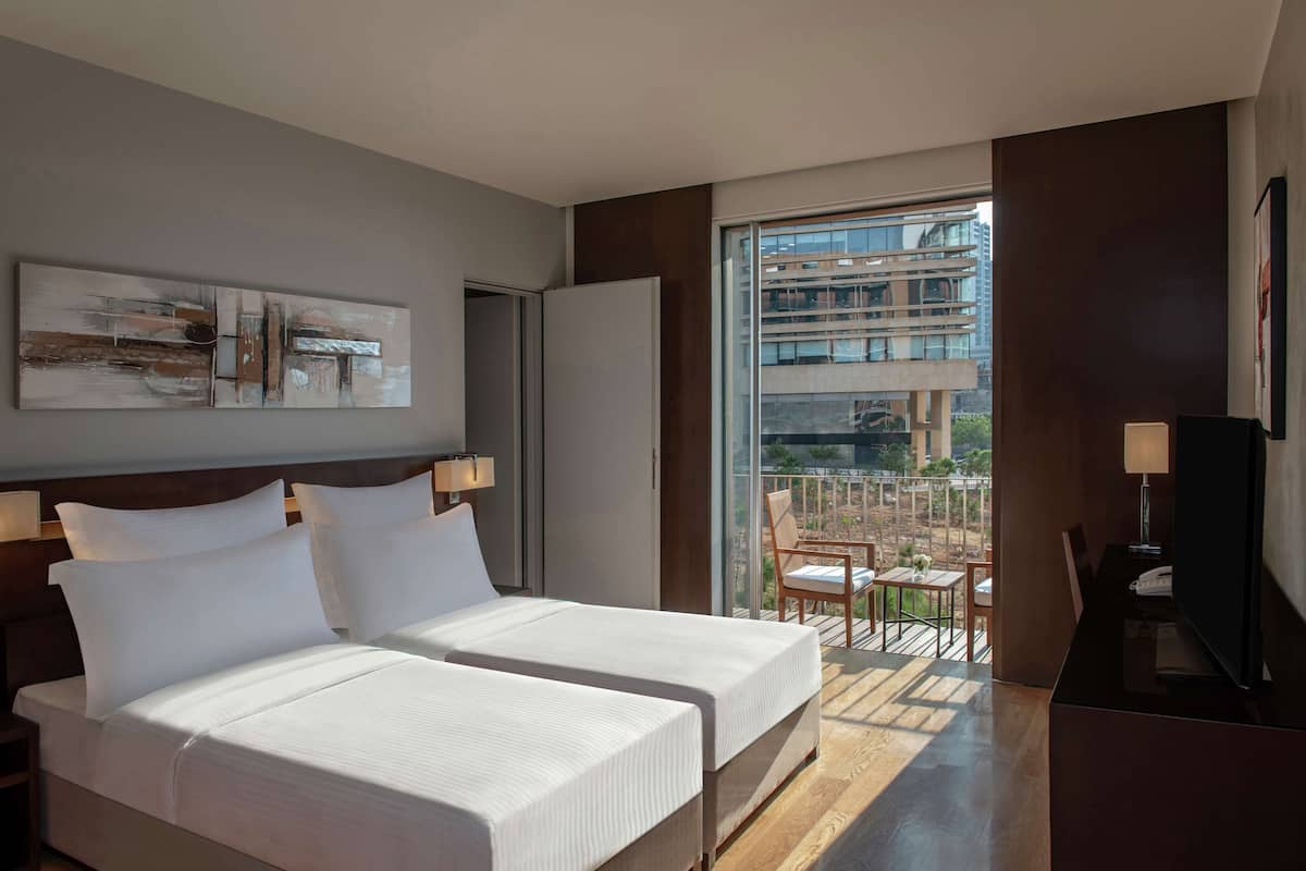 A hotel room with two beds, a balcony with a view of buildings, and a large window.