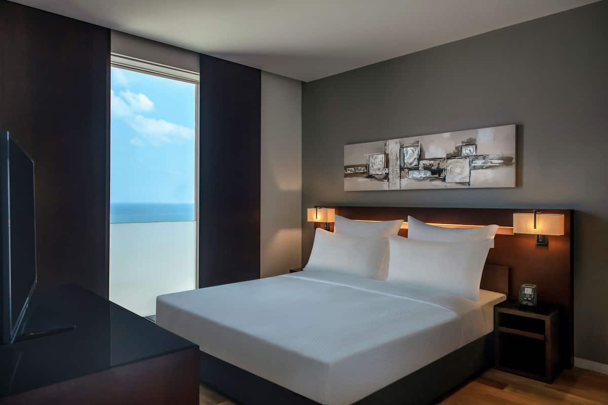 A modern hotel room with a large bed, a desk, and a view of the sky.