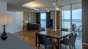 A modern living room with a wooden dining table, dark chairs, a large window with a view of the sea, and a ceiling light fixture. - Hilton Beirut Downtown (Beirut)