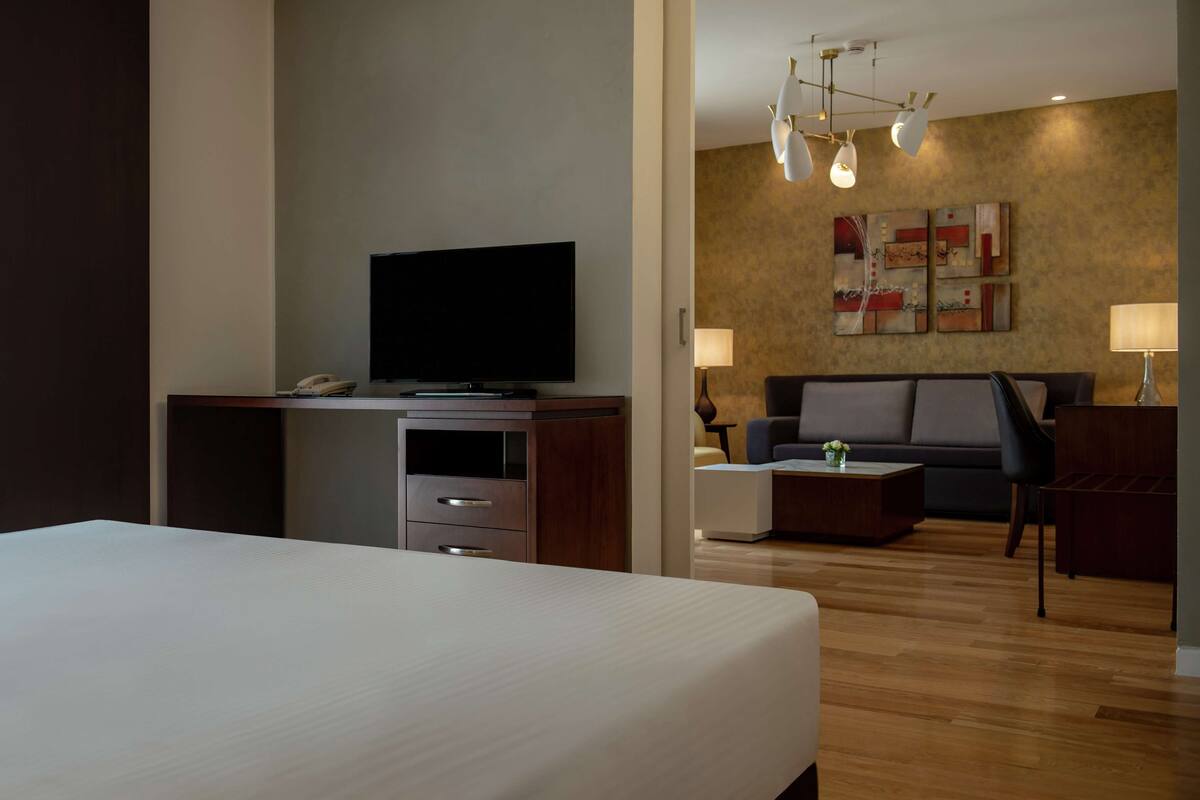 A hotel room with a large bed, a TV on a wooden stand, a sofa, a coffee table, and a lamp.