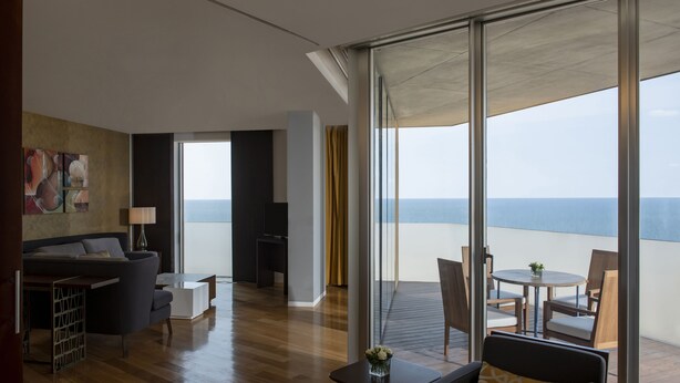 A modern hotel room with a balcony, a sofa, a dining table, and a TV. - Hilton Beirut Downtown (Beirut)