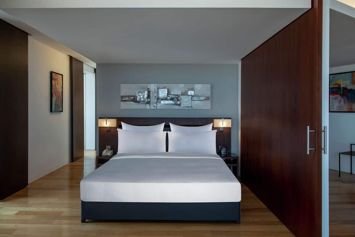 A modern hotel room with a large bed, wooden flooring, and a painting above the bed.