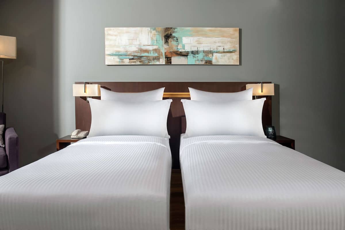 A double bed with white linens, two bedside tables with lamps, a telephone, and a painting on the wall.