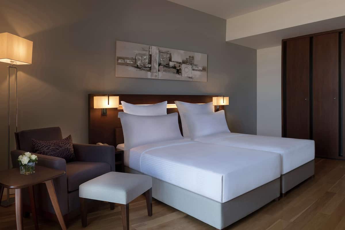 A modern hotel room with a large bed, a bedside table, a chair, and a wardrobe.