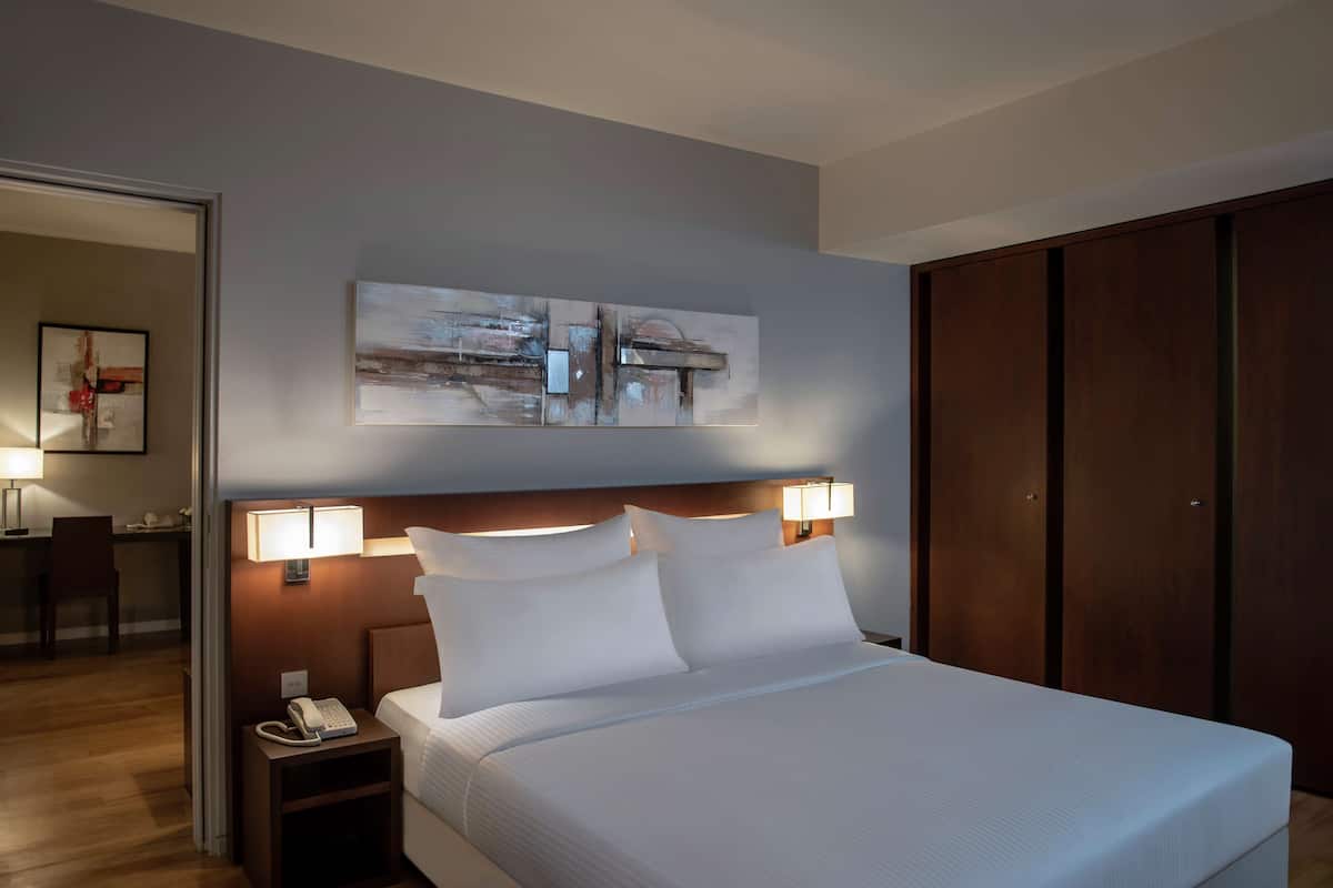 A hotel room with a large bed, bedside lamps, a desk with a chair, and a wardrobe.