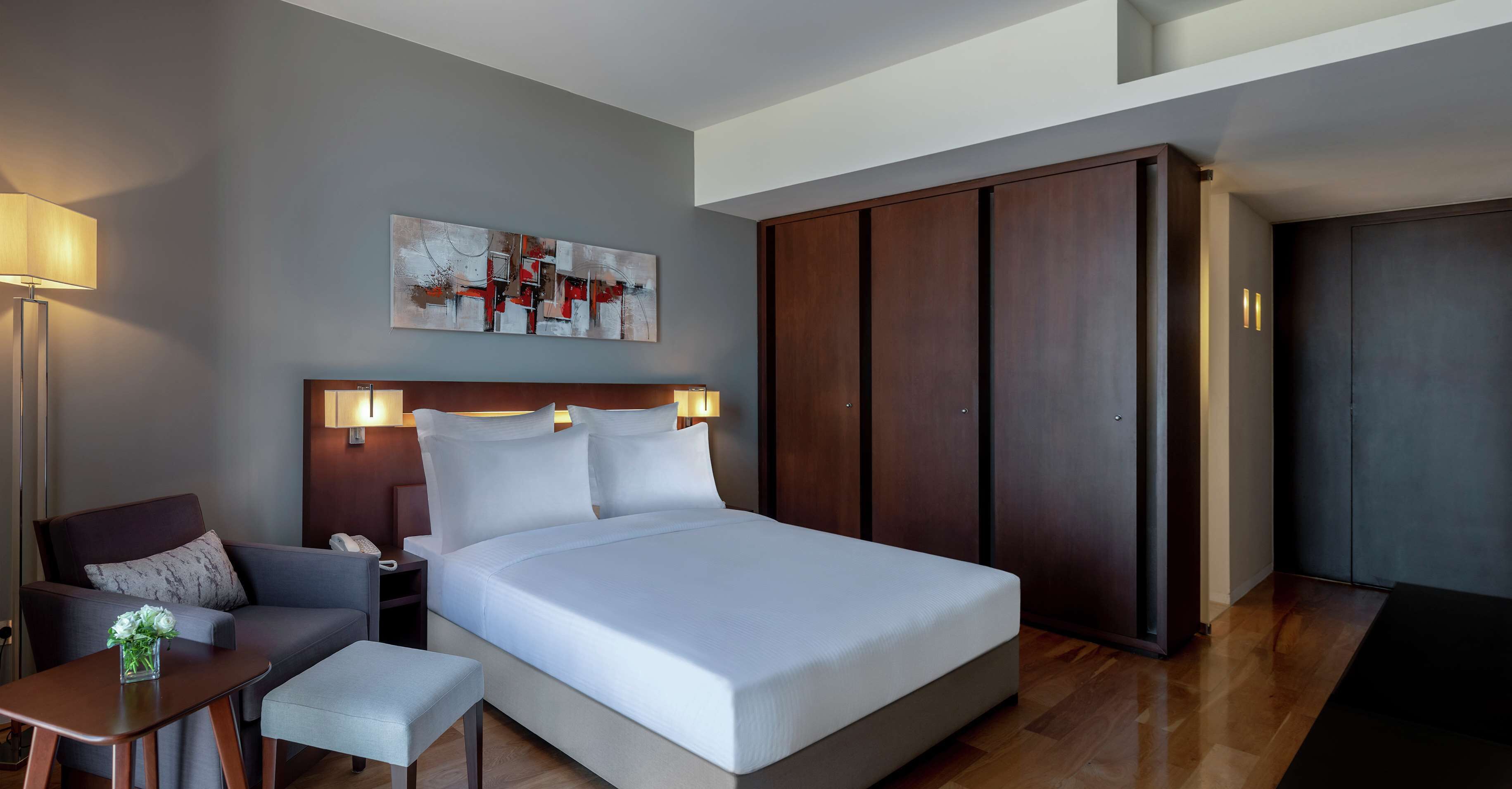 Een moderne hotelkamer met een groot bed, een bureau met lamp, een bank en een kledingkast.