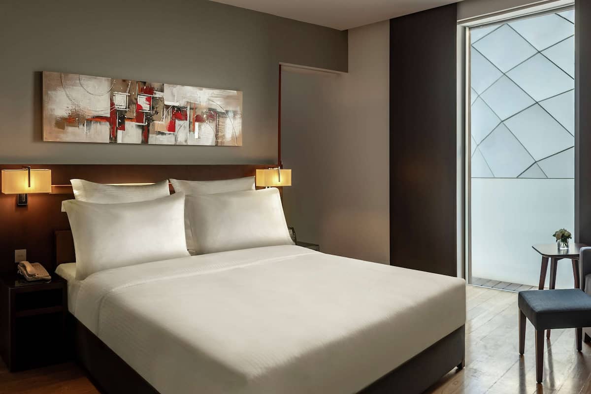 A hotel room with a large bed, two bedside lamps, a painting on the wall, and a view through a window.