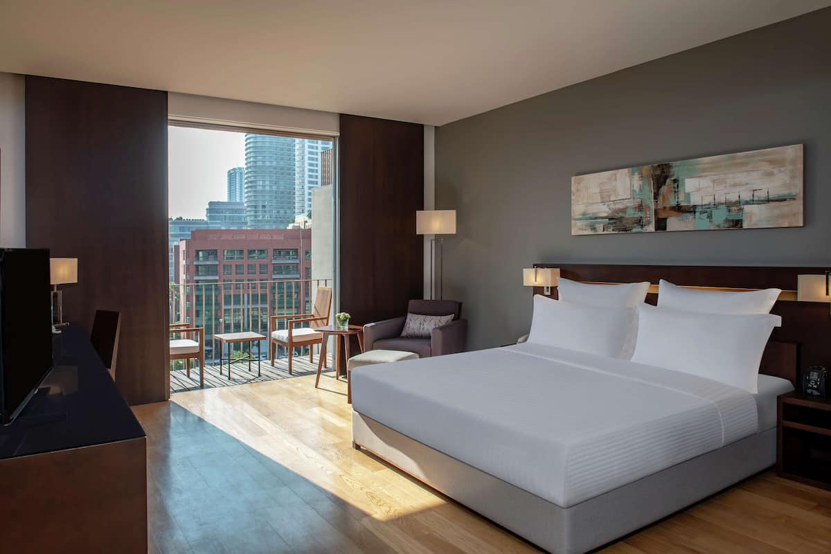 A modern hotel room with a large bed, a desk, a chair, and a balcony with a city view.