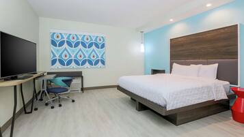 A modern hotel room with a bed, desk, chair, and a large TV.