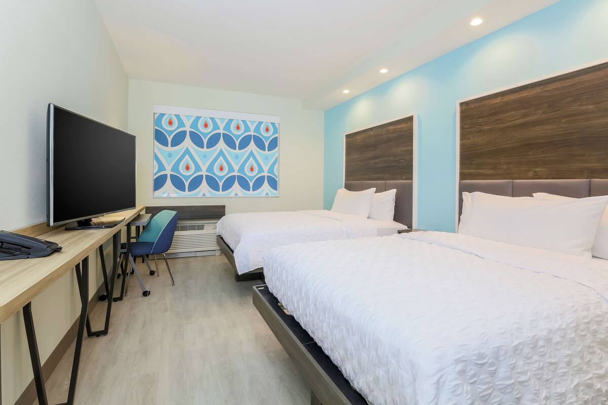 A hotel room with two beds, a desk with a computer, a TV, and a patterned wall decoration.