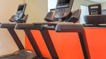 Three treadmills with digital screens and a red wall in the background.