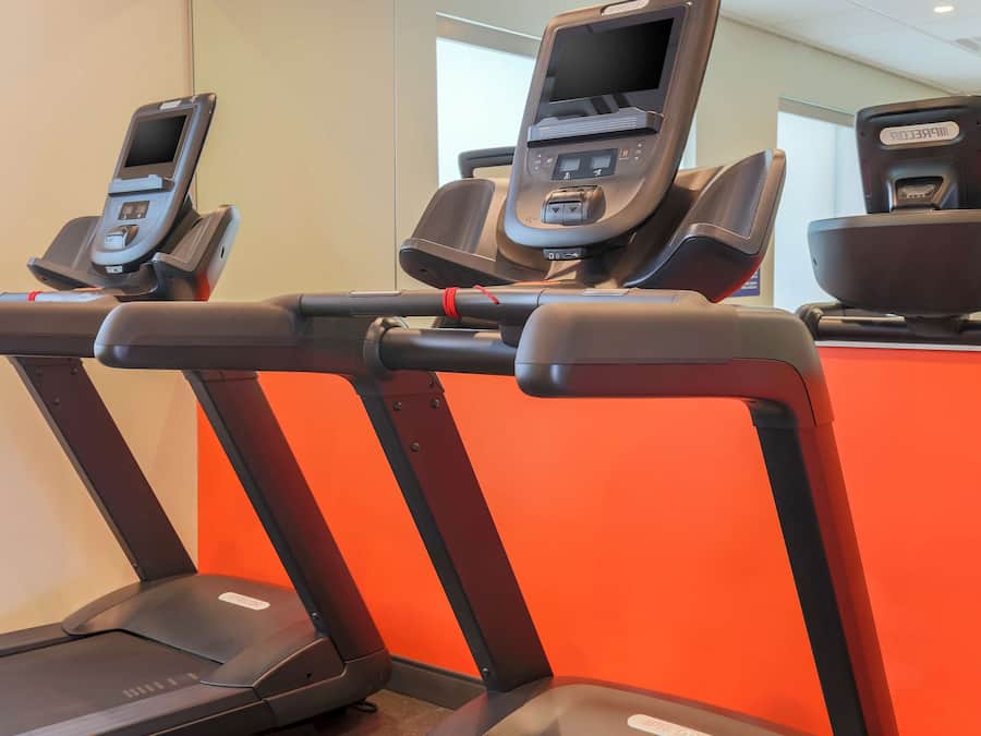 Three treadmills with digital screens and a red wall in the background.
