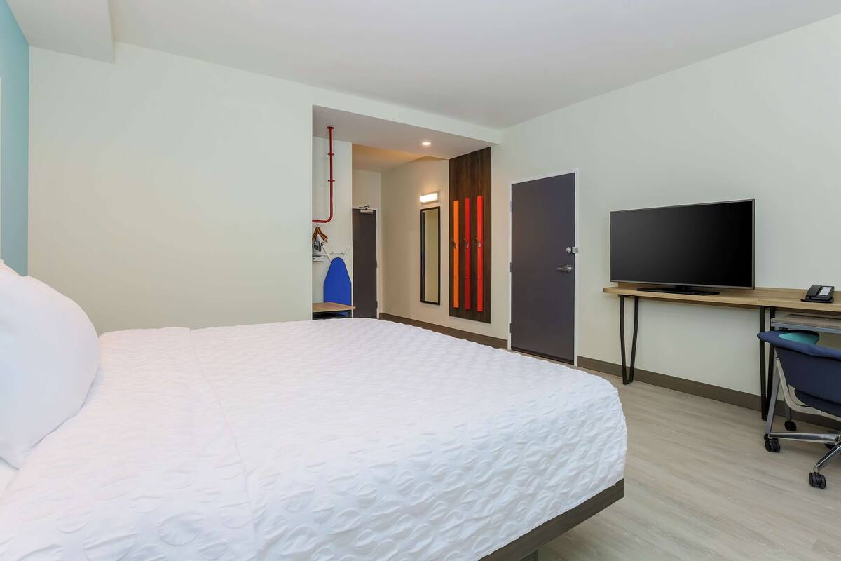 A hotel room with a large bed, a desk with a flat-screen TV, and a chair.
