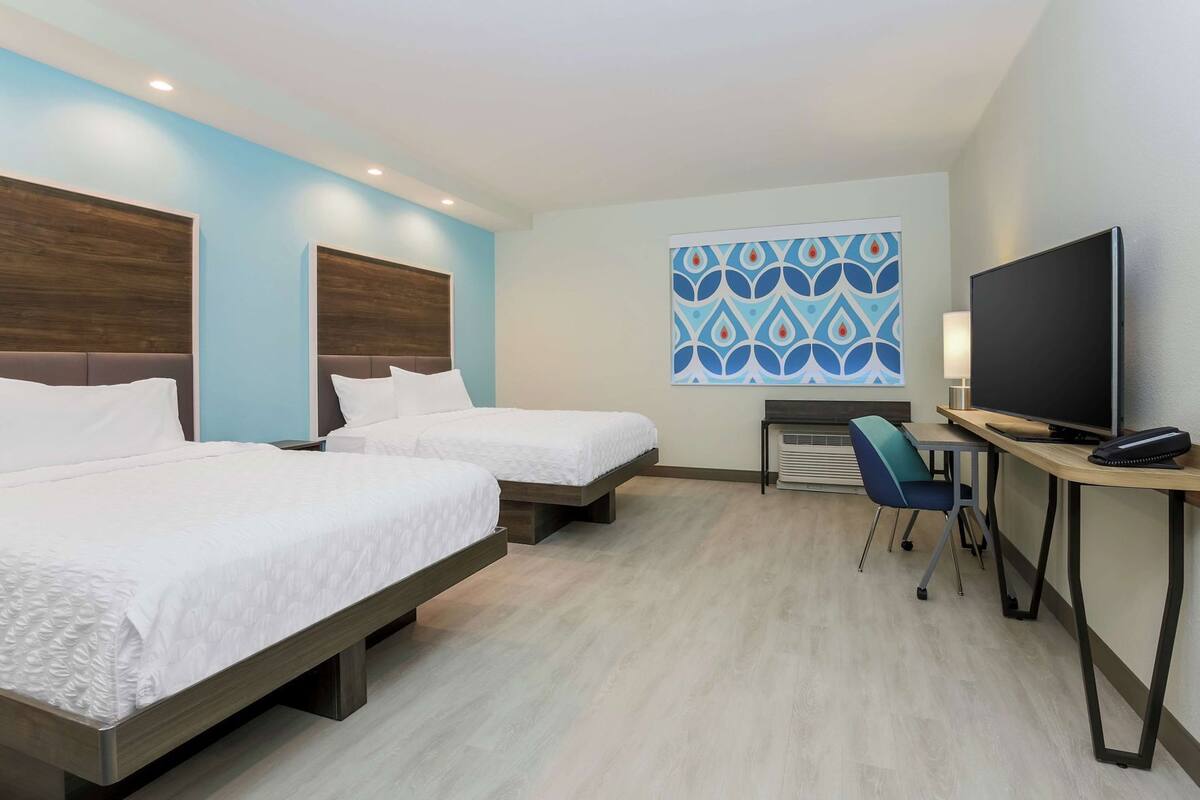 A hotel room with two beds, a desk with a television, and a patterned wall.