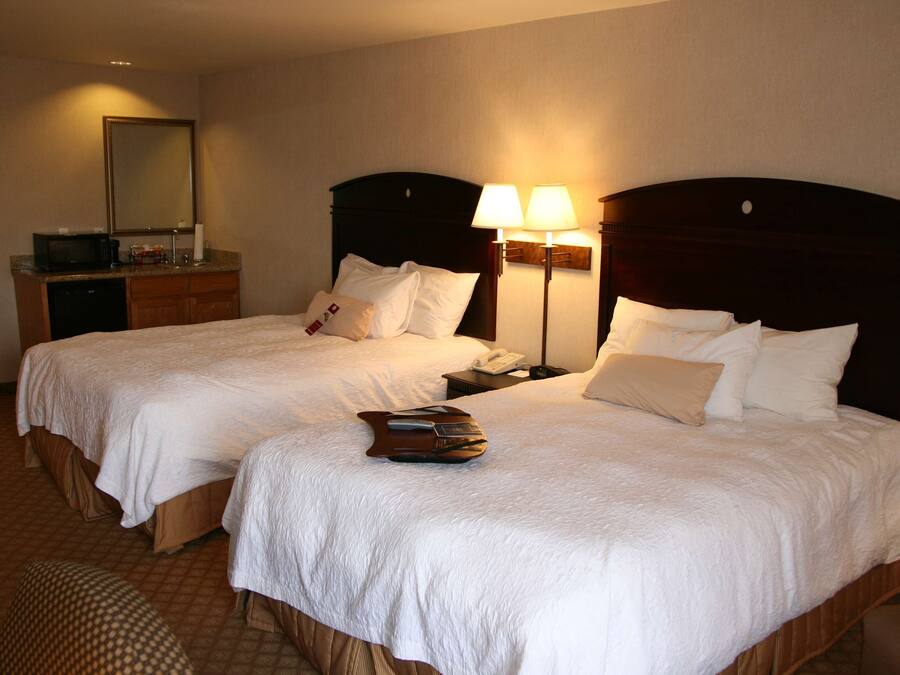 A hotel room with two beds, a desk with a microwave, a telephone, and two bedside lamps.