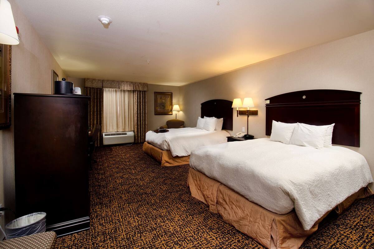Ein Hotelzimmer mit zwei Betten, einem Schminktisch, einem Schreibtisch und einer Lampe.