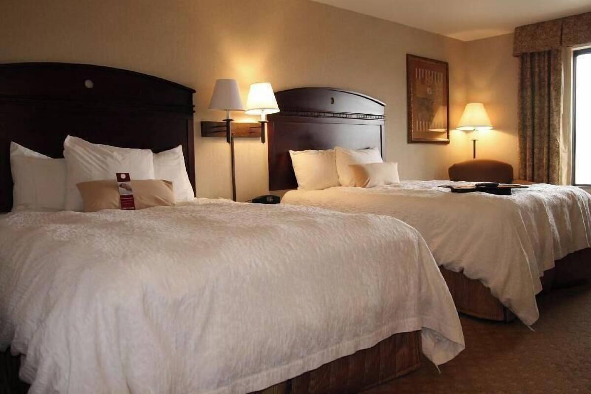 Ein Hotelzimmer mit zwei Betten, jeweils mit Kopfteil, Nachttischlampen und einem Nachttisch.