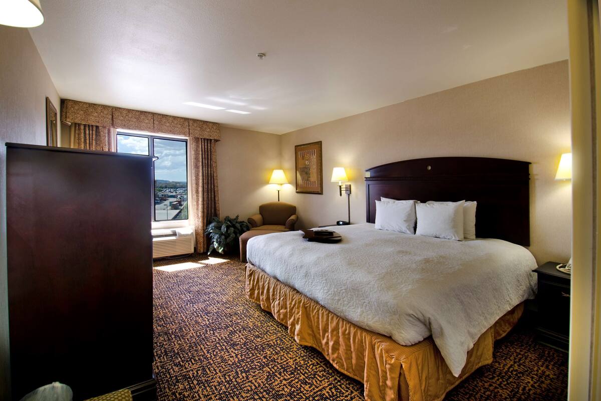 Ein Hotelzimmer mit einem großen Bett, einem Sessel, einem Schreibtisch und Blick auf die Stadt.