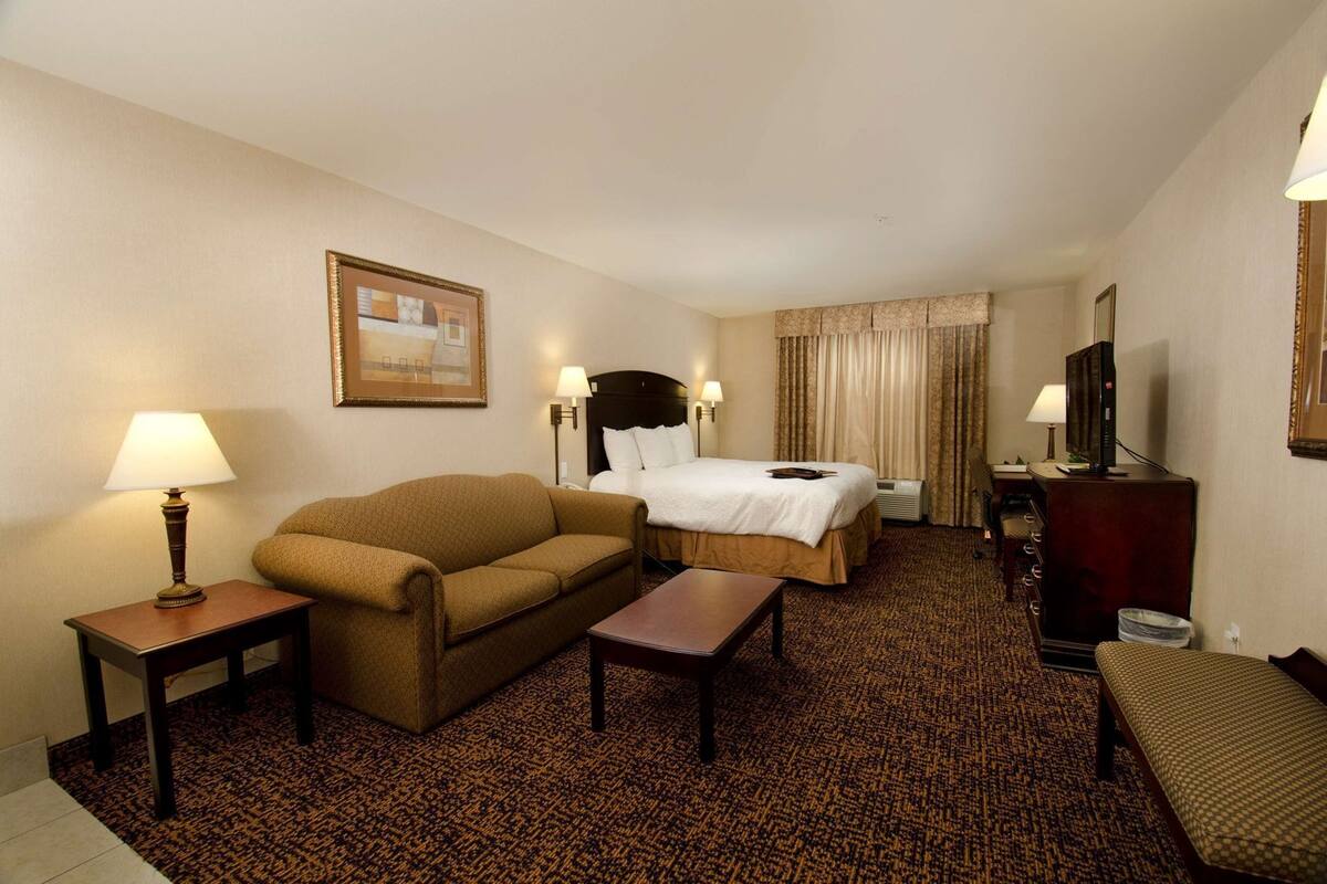 Ein Hotelzimmer mit Bett, Sofa, Schreibtisch, Fernseher und einem Bild an der Wand.