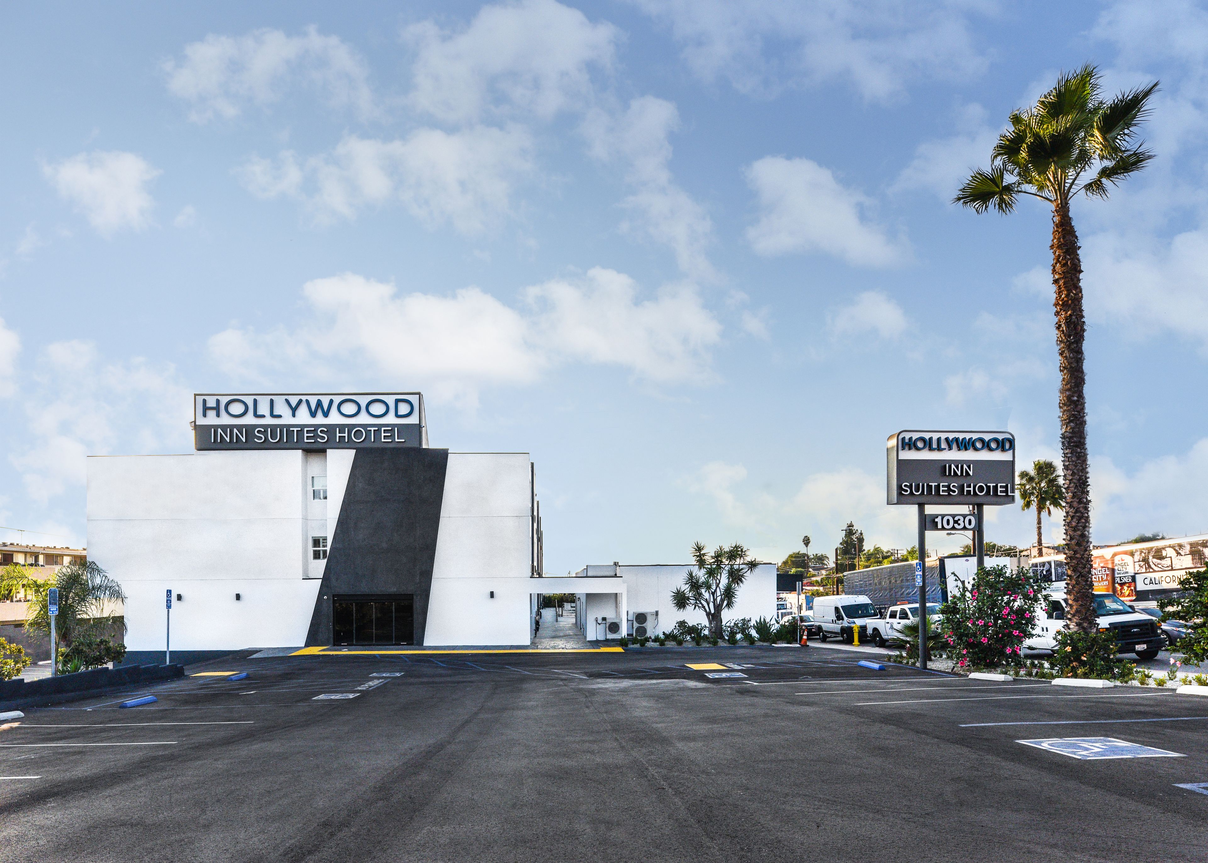 A modern building with a sign reading "Hollywood Inn Suites Hotel" and a parking lot in front.